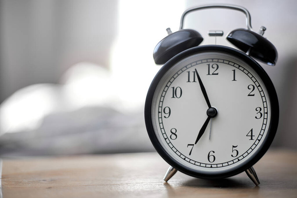 Vintage black alarm clock on bedroom. Morning time background concept with copy space. - Фото, изображение