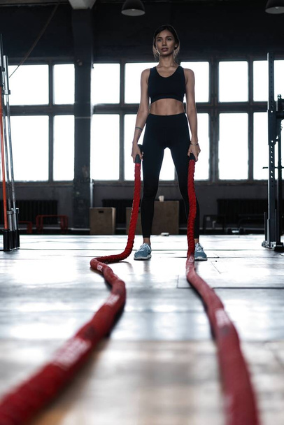 Νεαρή γυναίκα κάνει προπόνηση δύναμης χρησιμοποιώντας βαριά σχοινιά στο γυμναστήριο - Φωτογραφία, εικόνα