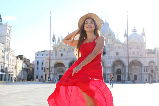 Ευτυχισμένη όμορφη γυναίκα με κομψό κόκκινο φόρεμα χορεύει στην πλατεία του Αγίου Μάρκου στη Βενετία της Ιταλίας. Αρκετά σέξι μοντέλο κορίτσι που ποζάρει στη Βενετία, Ιταλία. - Φωτογραφία, εικόνα