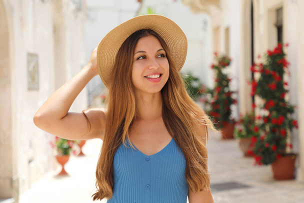 Портрет веселой туристки на старинной улице в старом городе. Привлекательная женщина в соломенной шляпе и синем платье наслаждается одиноким отдыхом в Европе. Концепция туризма и путешествия. - Фото, изображение