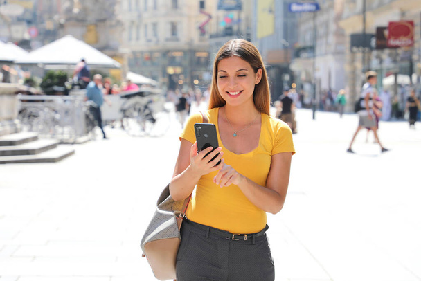 Прекрасна усміхнена жінка, яка ходить по вулиці Грабен у Відні, друкуючи на смартфоні - Фото, зображення