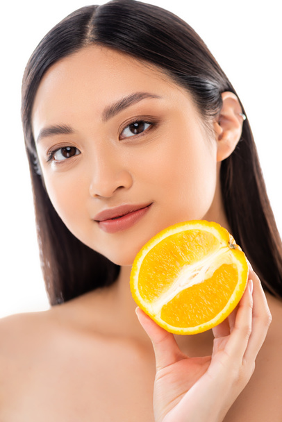 junge asiatische Frau blickt in die Kamera, während sie die Hälfte der reifen Orange isoliert auf weiß hält - Foto, Bild