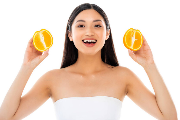excited asian woman looking at camera while holding halves of juicy orange isolated on white - Foto, immagini