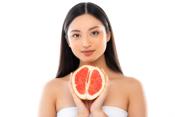 junge asiatische Frau blickt in die Kamera, während sie die Hälfte der Grapefruit isoliert auf weiß hält - Foto, Bild