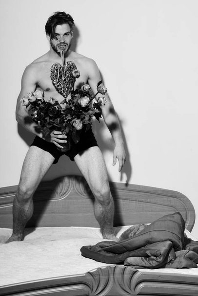 bearded macho man with roses on bed near red blanket holding orange roses - Foto, afbeelding