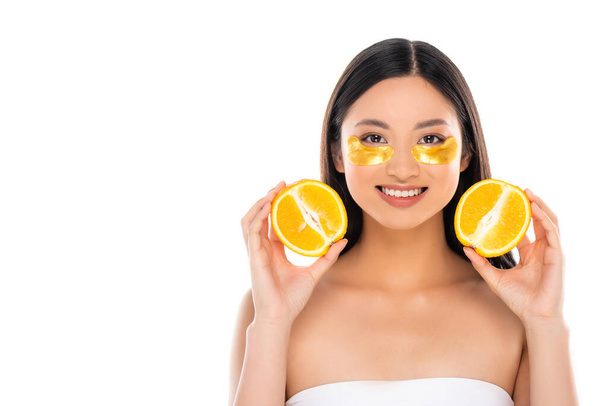 顔に黄金の眼帯を持つ若いアジア系女性は白で隔離された新鮮なオレンジの半分を持っている - 写真・画像