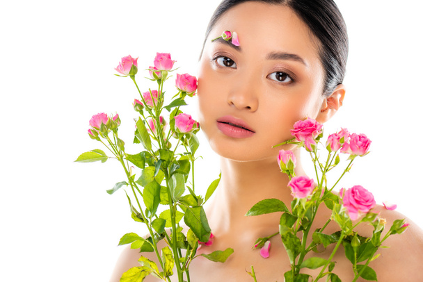 nude asian woman with floral decor on face near pink, tiny roses isolated on white - Photo, Image