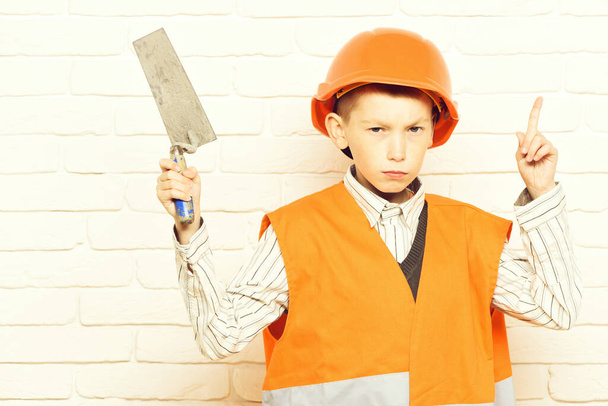 young cute builder boy on white brick wall background - Foto, afbeelding