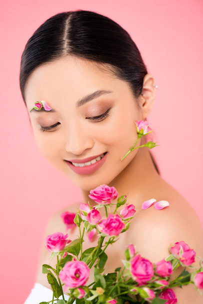 jovem mulher asiática com rosas minúsculas e decoração floral no rosto isolado no rosa - Foto, Imagem