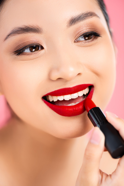Nahaufnahme der asiatischen Frau, die roten Lippenstift isoliert auf rosa aufträgt - Foto, Bild