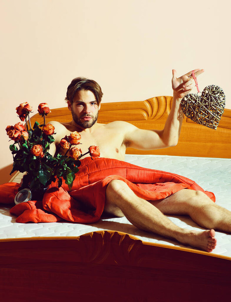 brodaty macho człowiek z róż na łóżku pod czerwony koc gospodarstwa bukiet - Zdjęcie, obraz