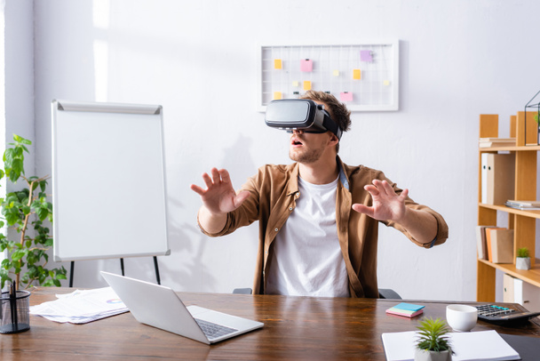excited businessman gesturing while using vr headset at workplace - Foto, Bild