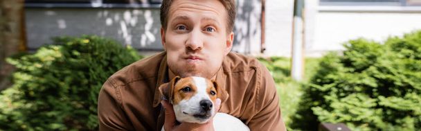 horizontal concept of man holding jack russell terrier dog, grimacing and puffing out cheeks - Photo, Image