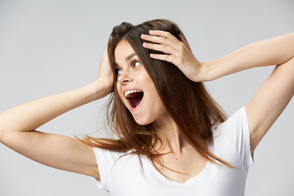 Mujer con la boca abierta sostiene su mirada cabeza al lado blanco camiseta emociones  - Foto, imagen