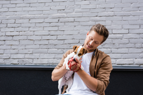 Man holding on hands jack russell terrier and leash on urban street  - Fotó, kép