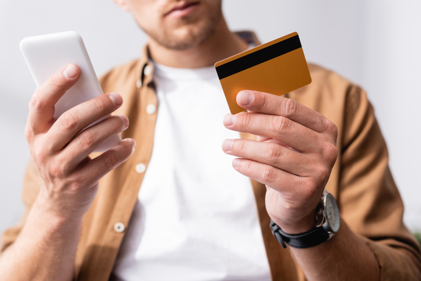 Selective focus of businessman holding credit card while using smartphone in office  - Fotoğraf, Görsel