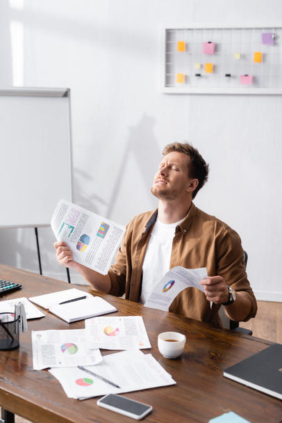 Выборочный фокус стрессового бизнесмена, держащего бумажную работу за столом  - Фото, изображение