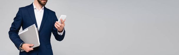 cropped view of businessman in blue blazer holding smartphone and folder isolated on grey, panoramic shot - Foto, Bild