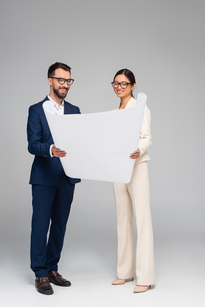 full length view of interracial couple of businesspeople looking at white paper on grey - Photo, Image