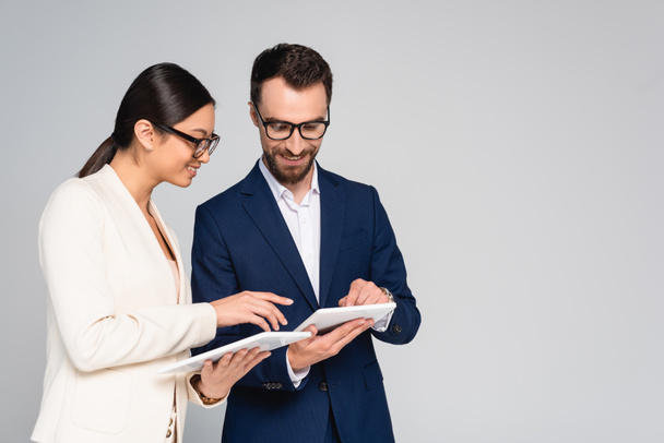 interracial couple of business colleagues in blazers and eyeglasses using digital tablets isolated on grey - Fotografie, Obrázek
