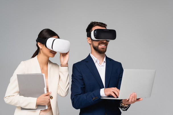 businesswoman touching vr headset near businessman using laptop isolated on grey - Foto, immagini