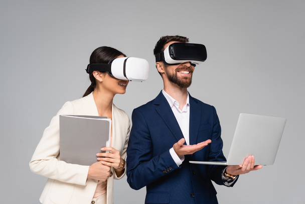 businessman pointing at laptop while using vr headsets together with business partner isolated on grey - Photo, Image
