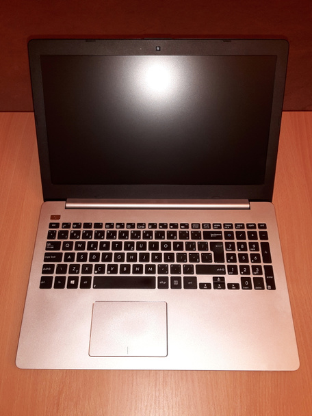 Laptop uitgezet, met lichtreflectie op display, open en gelegd op houten bureau, afbeelding - Foto, afbeelding