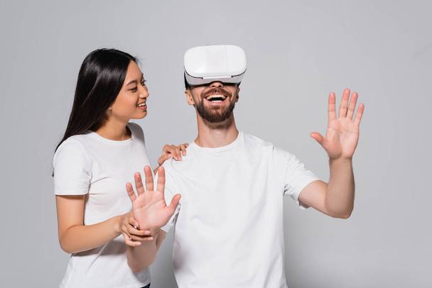 young asian woman touching excited boyfriend using vr headset and gesturing on grey - Fotografie, Obrázek