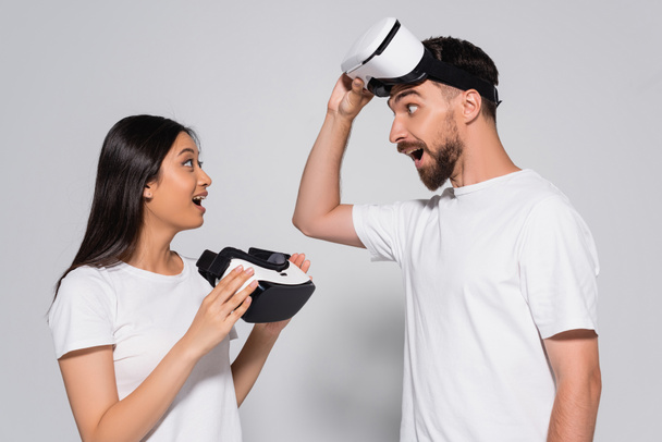 young asian woman in white t-shirt holding vr headset while looking at excited man on white - Foto, Imagem