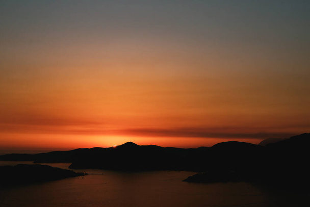 Orangefarbener Abendhimmel. Die Sonne geht hinter der Silhouette des Berges unter. - Foto, Bild
