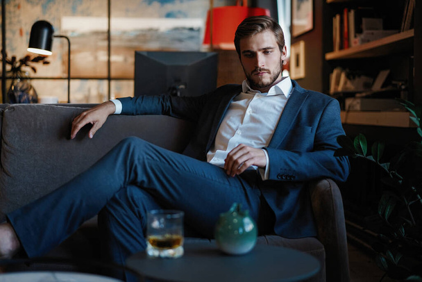 Young and charming businessman is thinking about business while sitting on the sofa in his modern office. - Fotó, kép