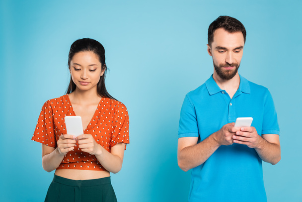 young asian woman in red blouse and bearded man in polo t-shirt using smartphones on blue - Foto, Bild