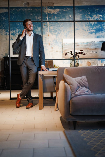 handsome businessman in suit standing and talking on smartphone in modern office. - Fotografie, Obrázek