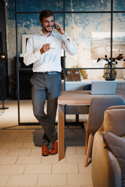 handsome businessman in suit standing and talking on smartphone in modern office. - Fotografie, Obrázek