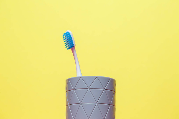 Een blauwe tandenborstel staat in een grijs glas. Begrip tandheelkundige verzorging - Foto, afbeelding
