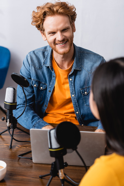 selective focus of excited redhead radio host interviewing brunette woman in studio - Foto, imagen