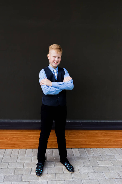 Το αγόρι με τη σχολική στολή ενάντια στο μαύρο τοίχο, πίσω στο σχολείο - Φωτογραφία, εικόνα