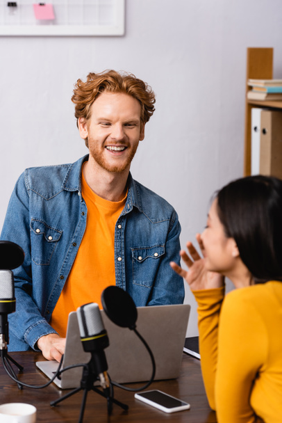 excited radio host laughing while interviewing young brunette woman in studio - Photo, Image