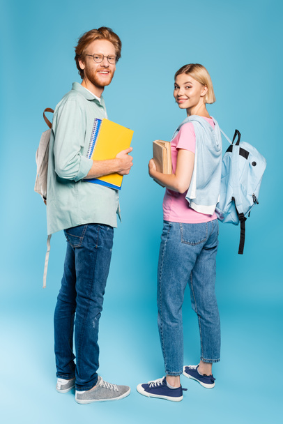students with backpacks holding notebooks and books while standing on blue  - Foto, imagen