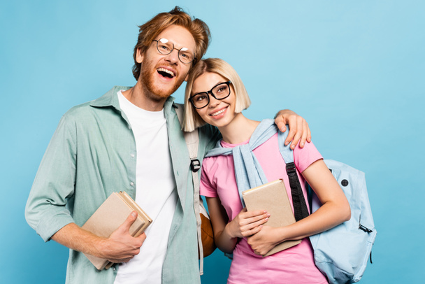 redhead man and blonde woman holding books and hugging on blue  - Foto, Bild