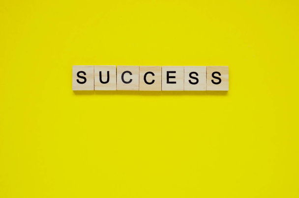 Word success. Wooden blocks with lettering on top of yellow background. Top view of wooden blocks with letters on yellow surface - Photo, Image