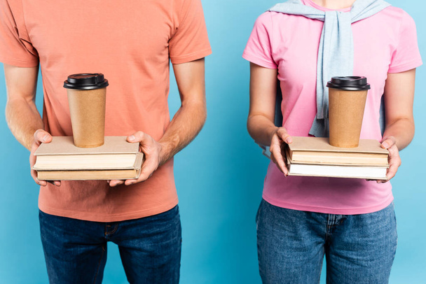 cropped view of students holding books with coffee to go on blue - Photo, Image