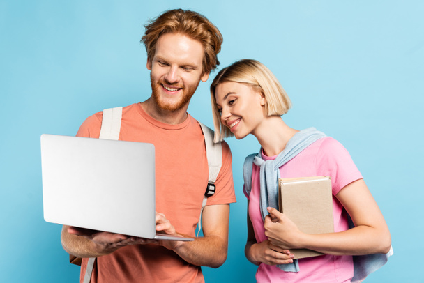redhead and blonde students looking at laptop on blue - Фото, изображение