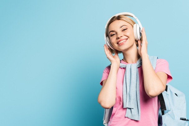 blonde student listening music in wireless headphones on blue - Photo, Image