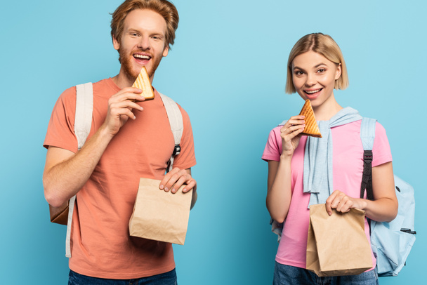 young students holding paper bags and eating toast bread on blue - Photo, Image