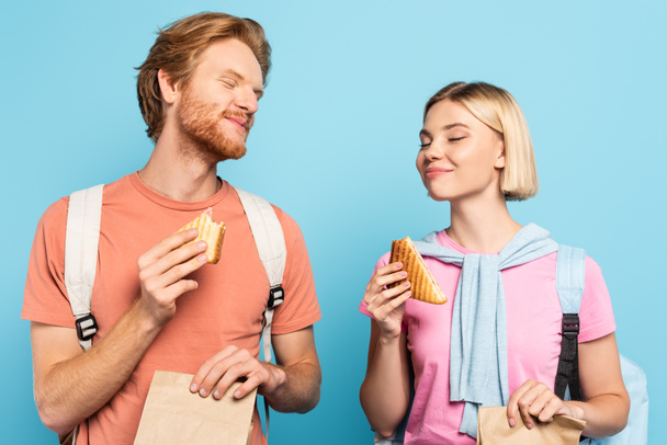 jóvenes estudiantes con los ojos cerrados sosteniendo bolsas de papel y sándwiches en azul - Foto, imagen