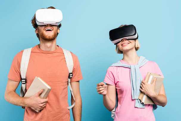 young students in virtual reality headsets holding books on blue - Photo, Image