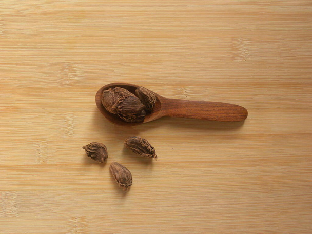 Colore nero grandi baccelli di semi di cardamomo su cucchiaio di legno - Foto, immagini