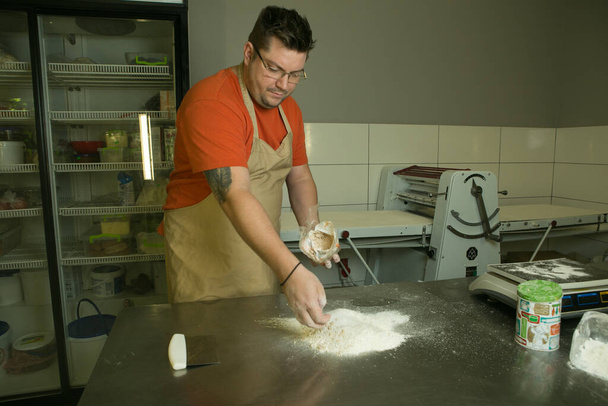 Η διαδικασία της παραγωγής ψωμιού. Ο σεφ ζυμώνει τη ζύμη με το χέρι. Ο σεφ προσθέτει αλεύρι.. - Φωτογραφία, εικόνα