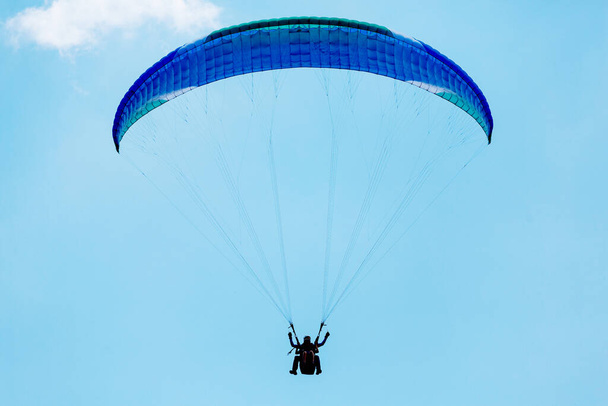 Blue Paraglider flying into the sky with clouds on a sunny day. - Photo, Image